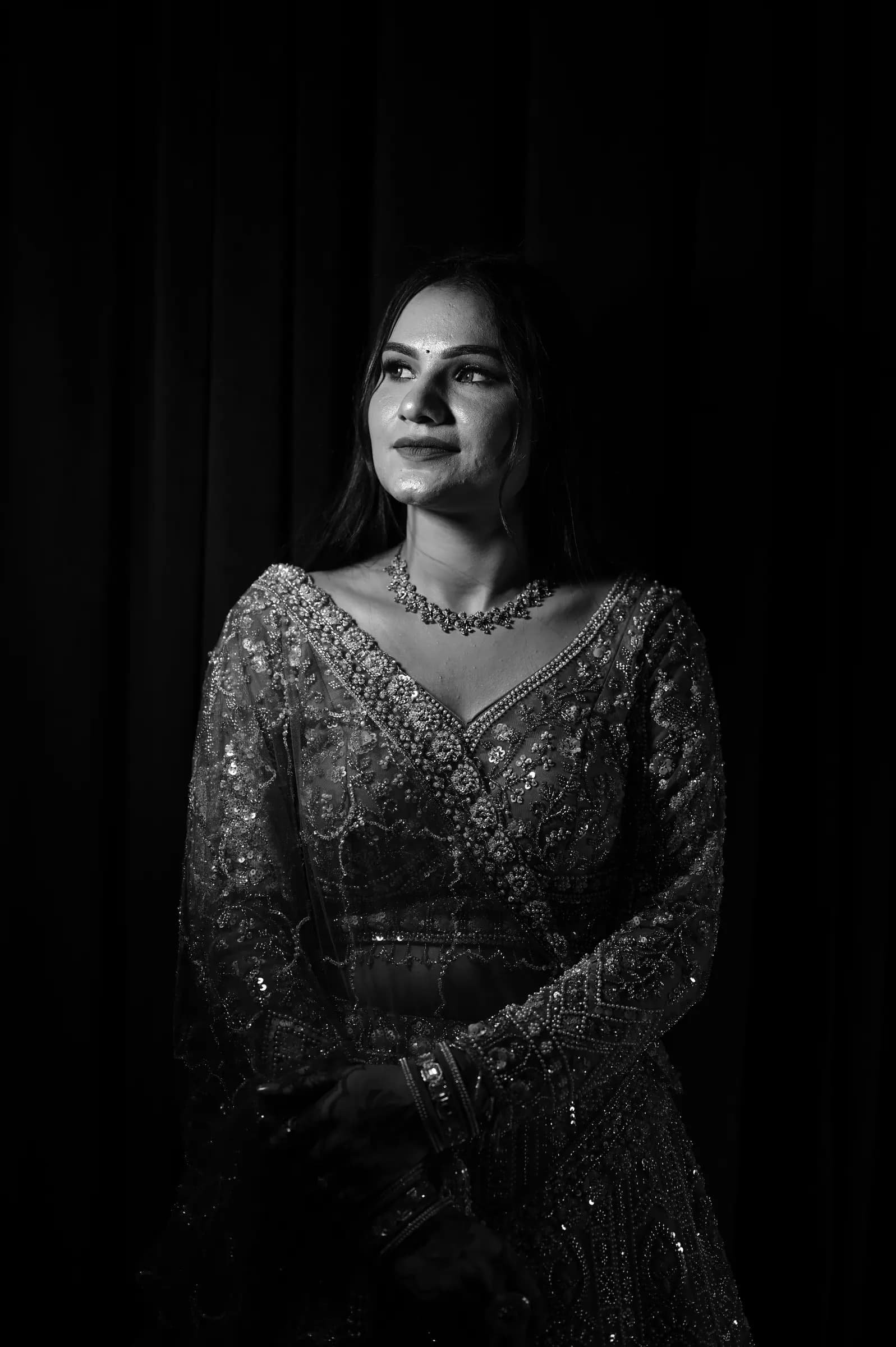 Black and white portrait of a woman in an embellished lehenga against a dark backdrop