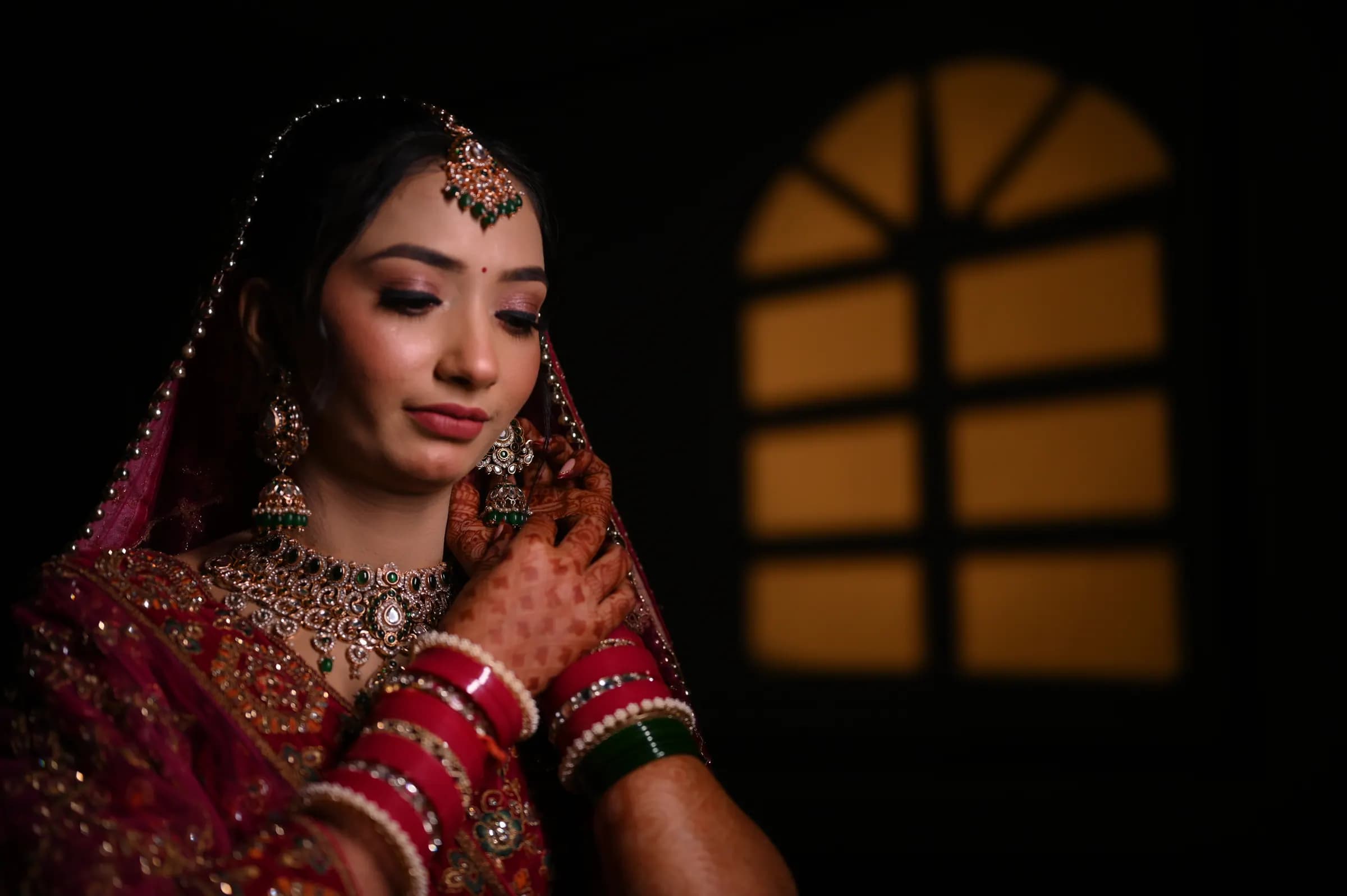 Bride adjusting her earrings beside a glowing arched window
