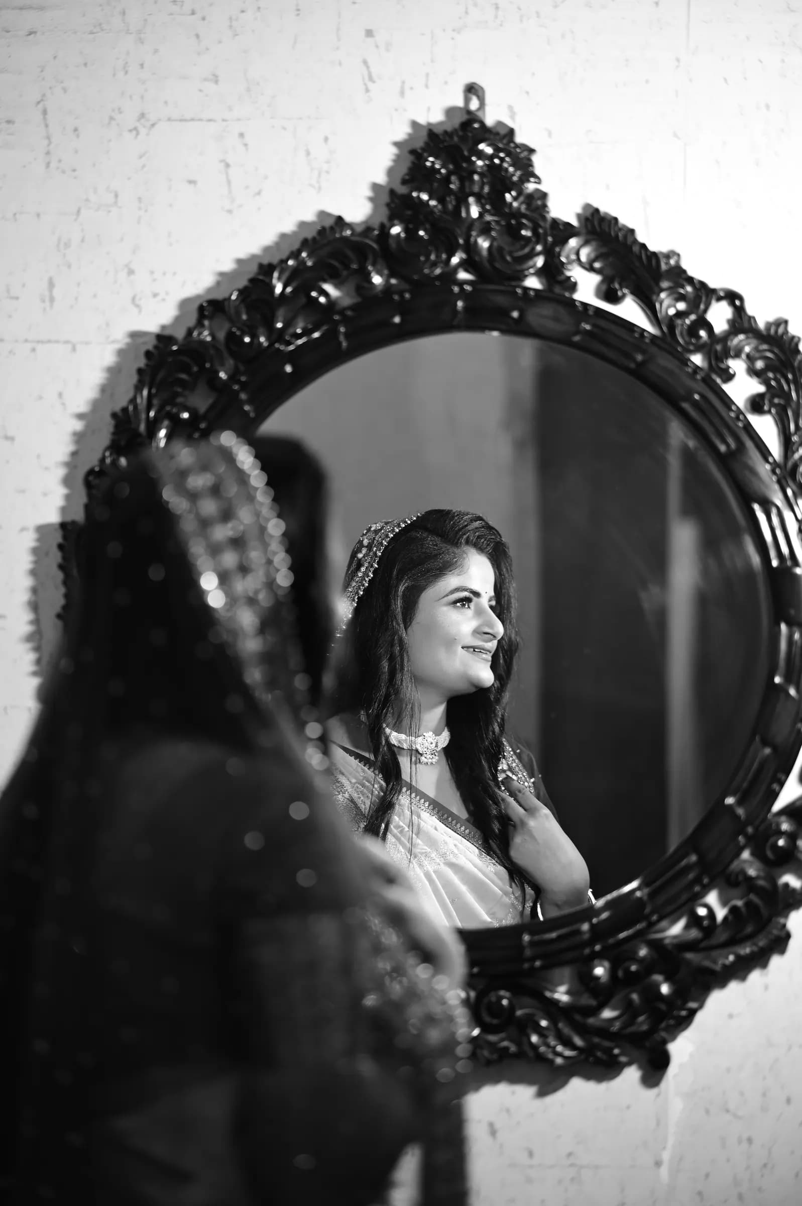Black and white portrait of a bride smiling at her reflection in an ornate mirror