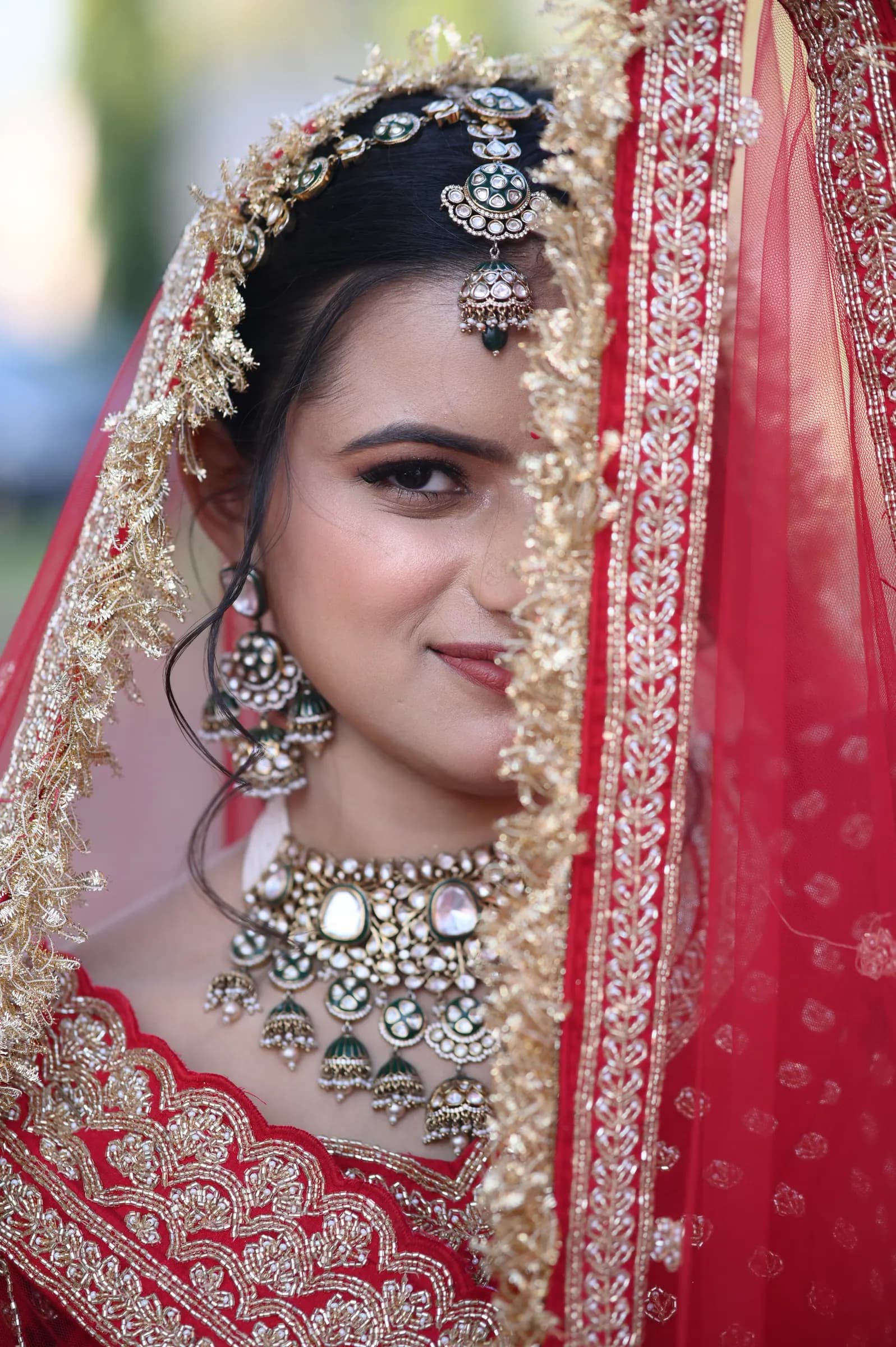 Close-up of a bride smiling from behind her embroidered red dupatta