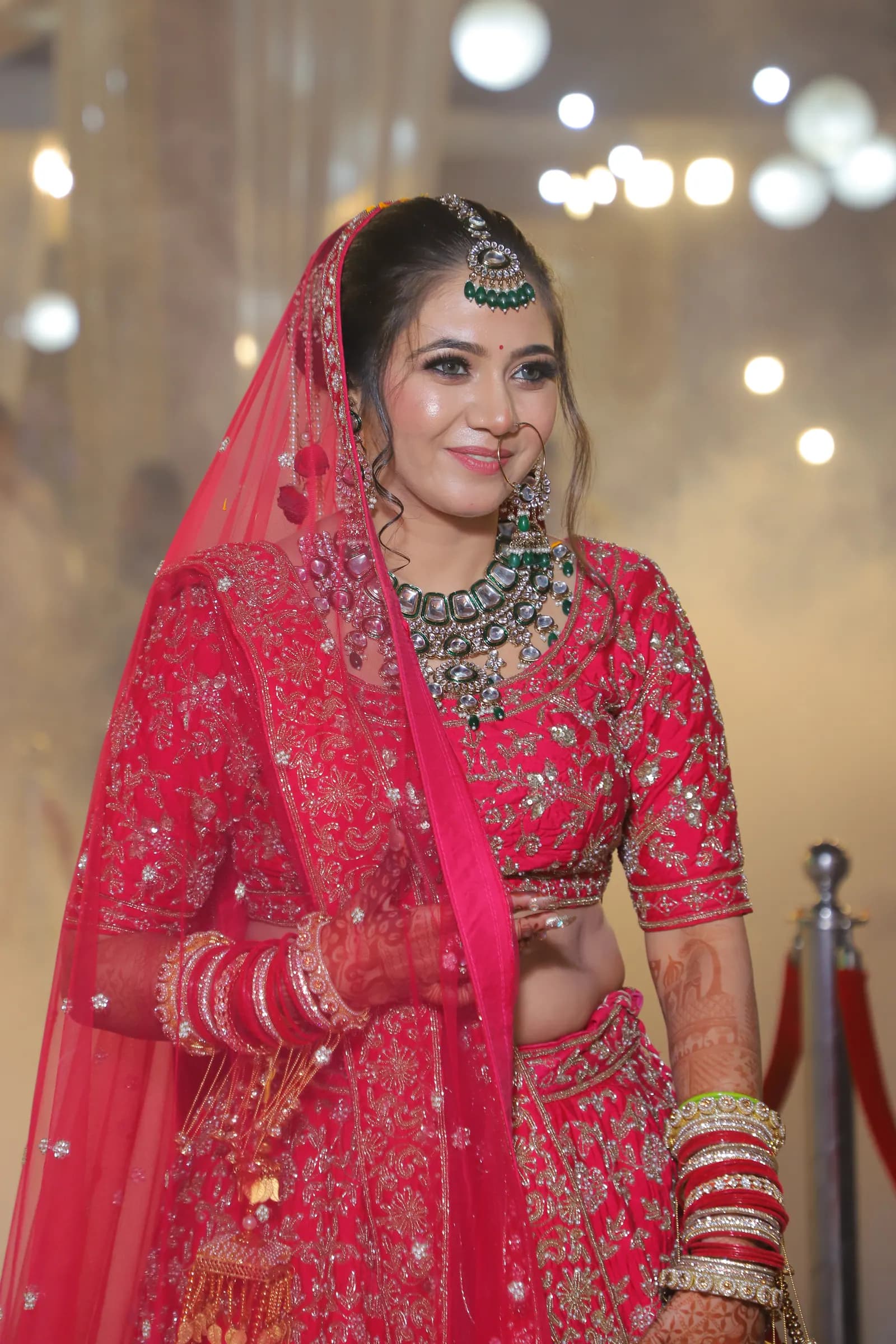 Bride in a red lehenga smiling, with soft venue lights behind her