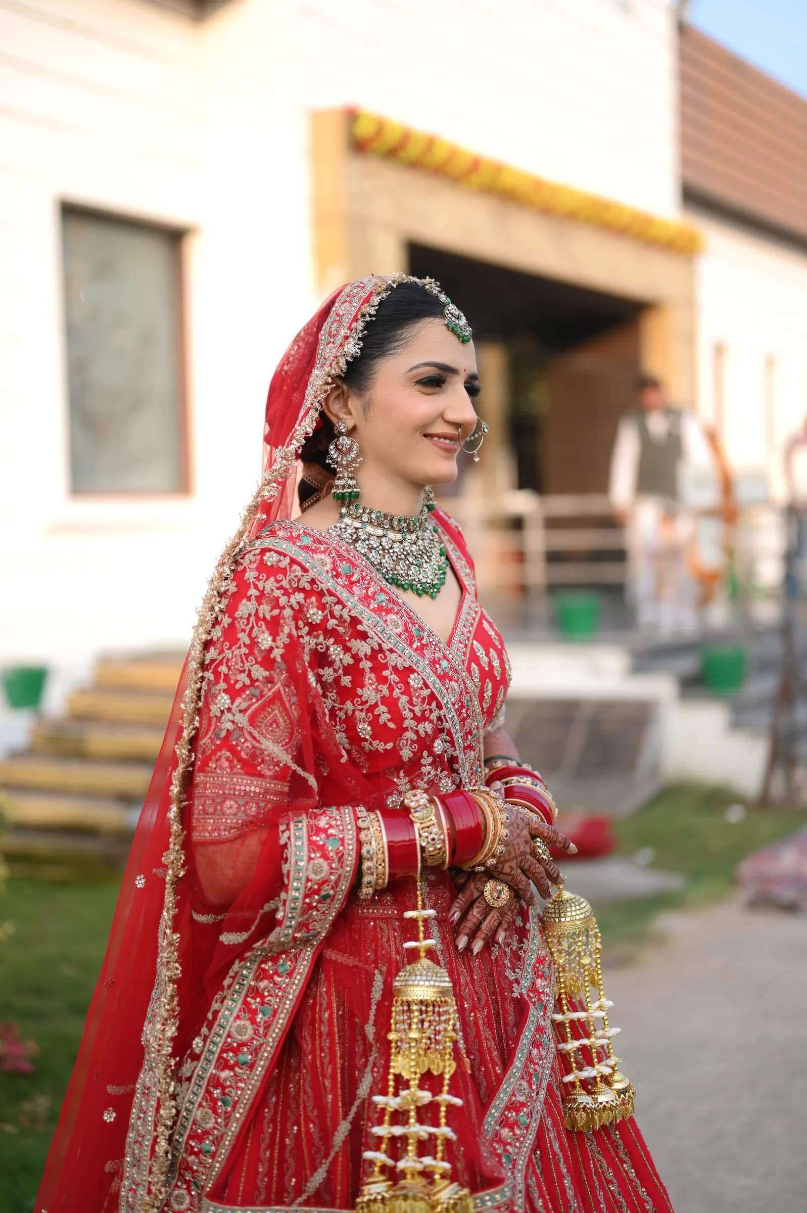 Bride in a red lehenga with gold kaleere posing outdoors
