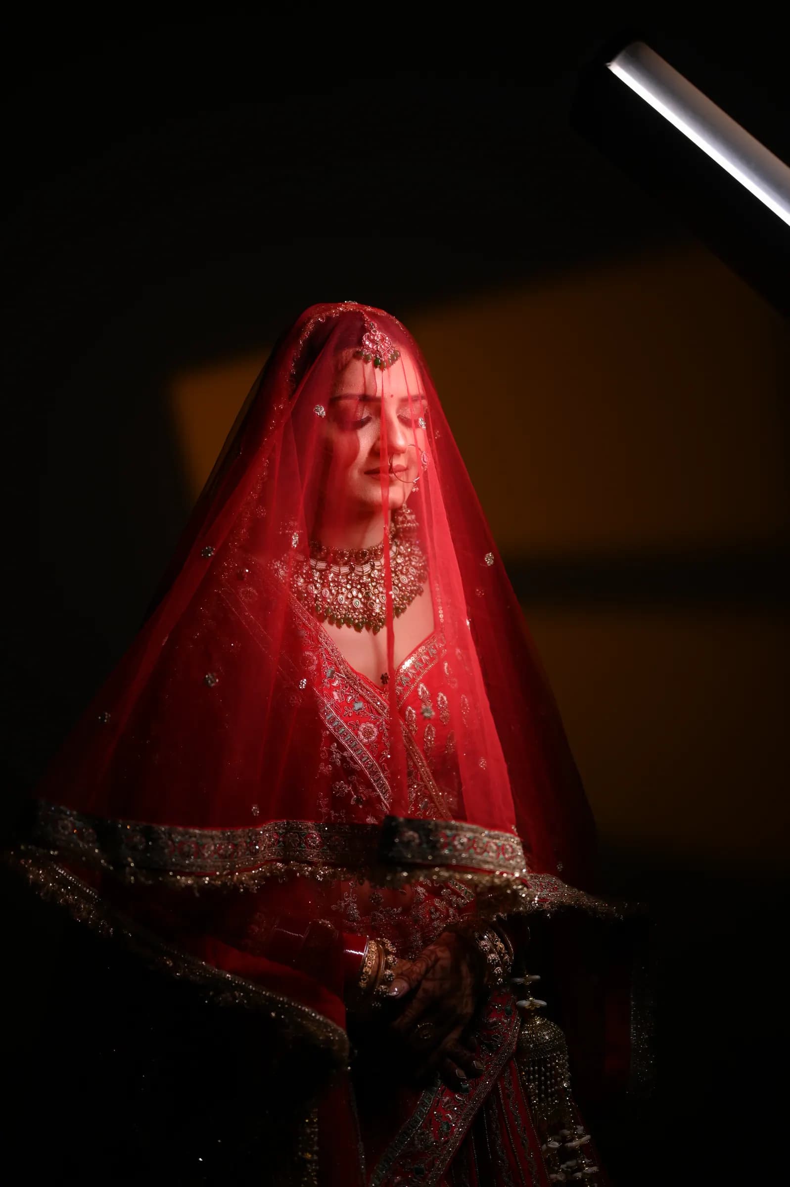 Bride under a sheer red veil in dramatic low light