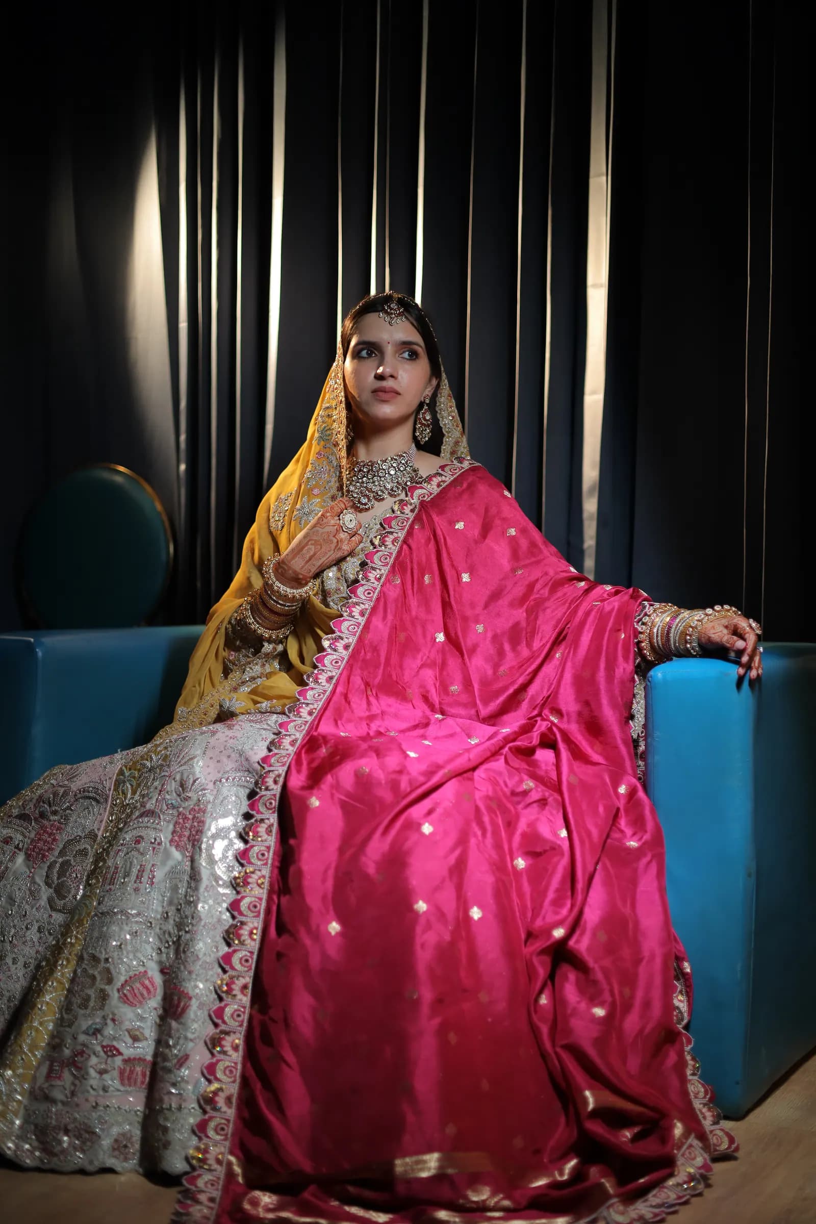 Bride seated on a blue velvet sofa in a pink and silver lehenga