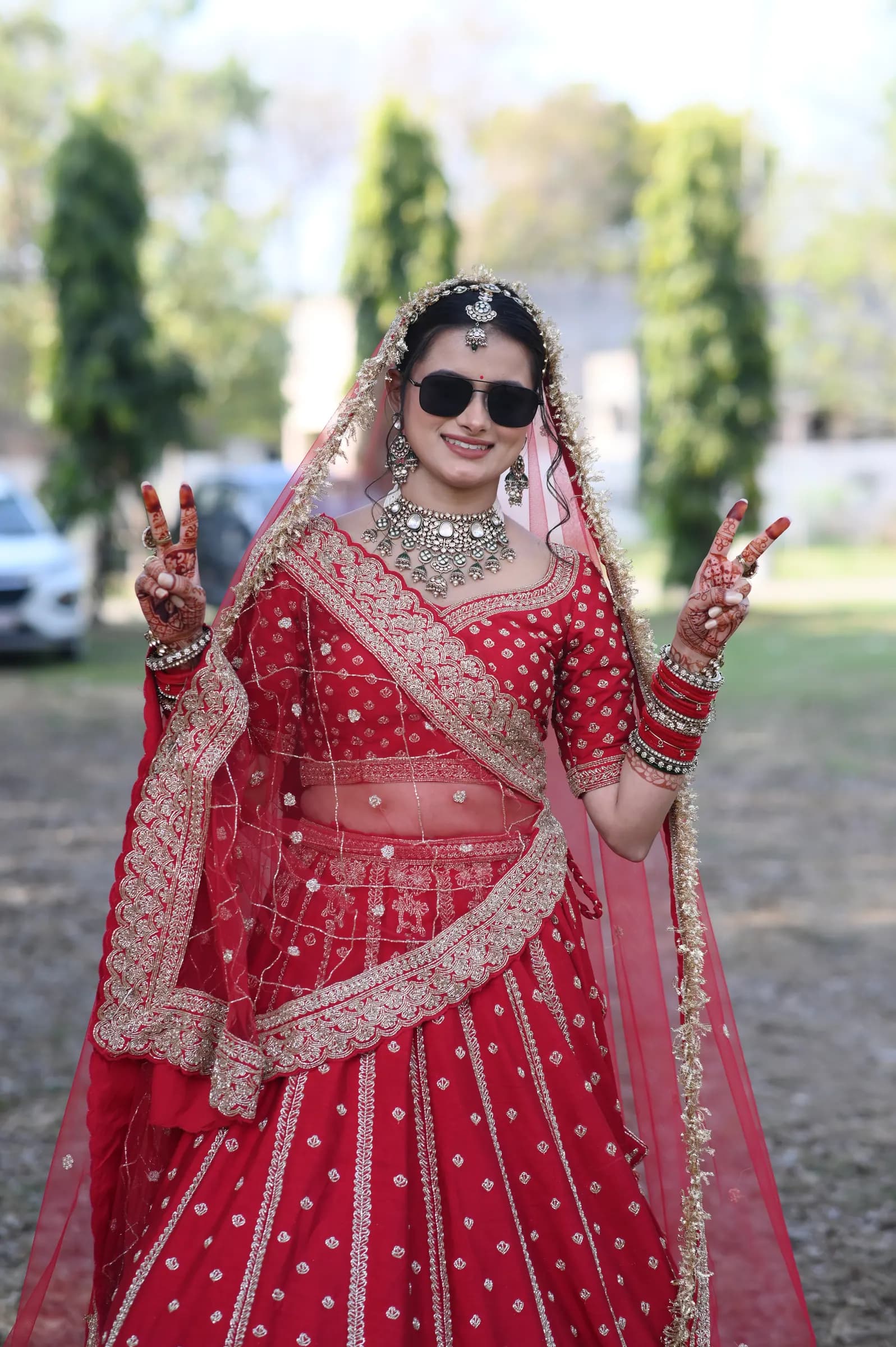 Bride in a red lehenga and sunglasses making peace signs, a fun candid portrait