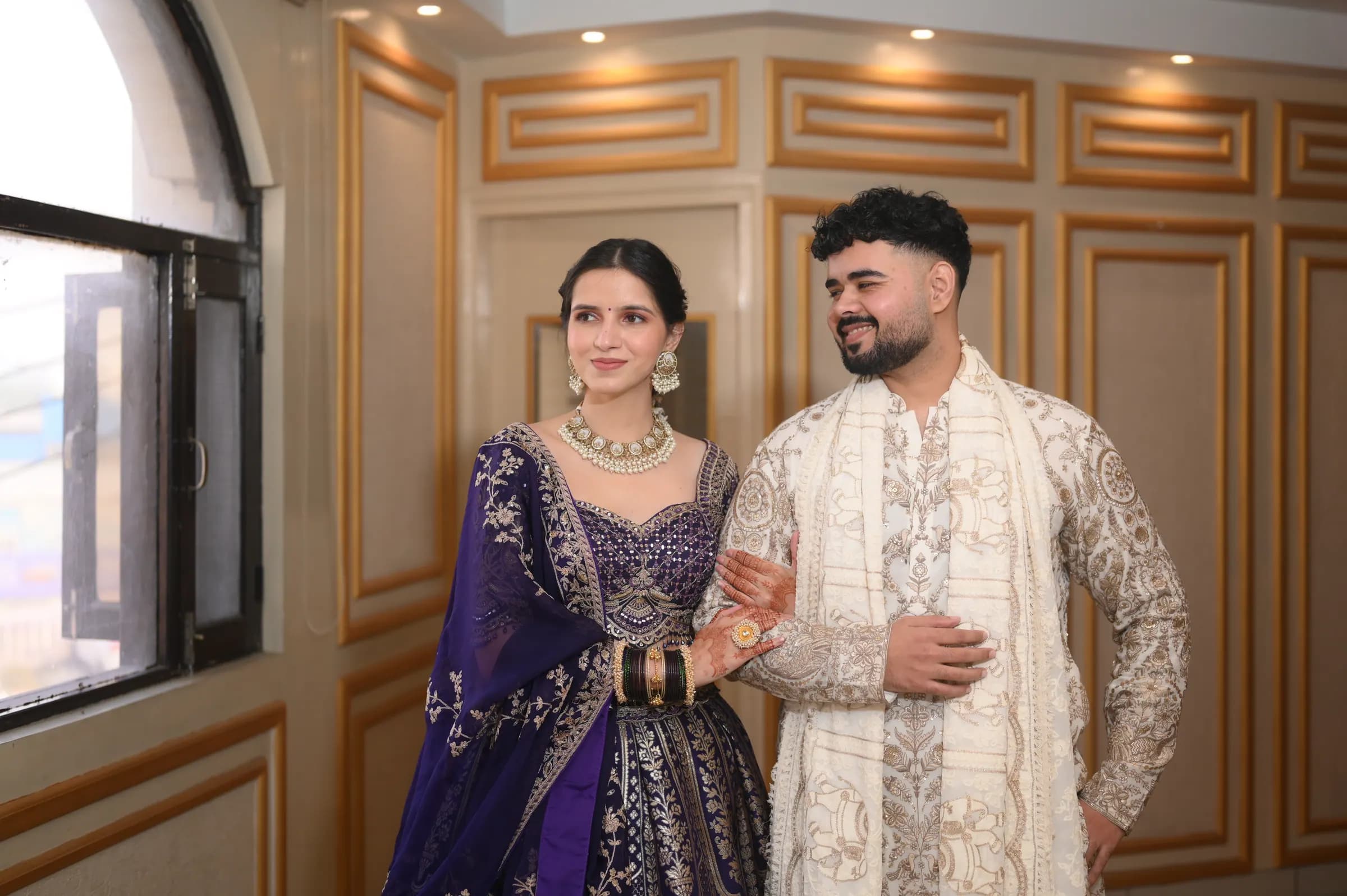 Couple smiling arm in arm beside a window in a gold-panelled room
