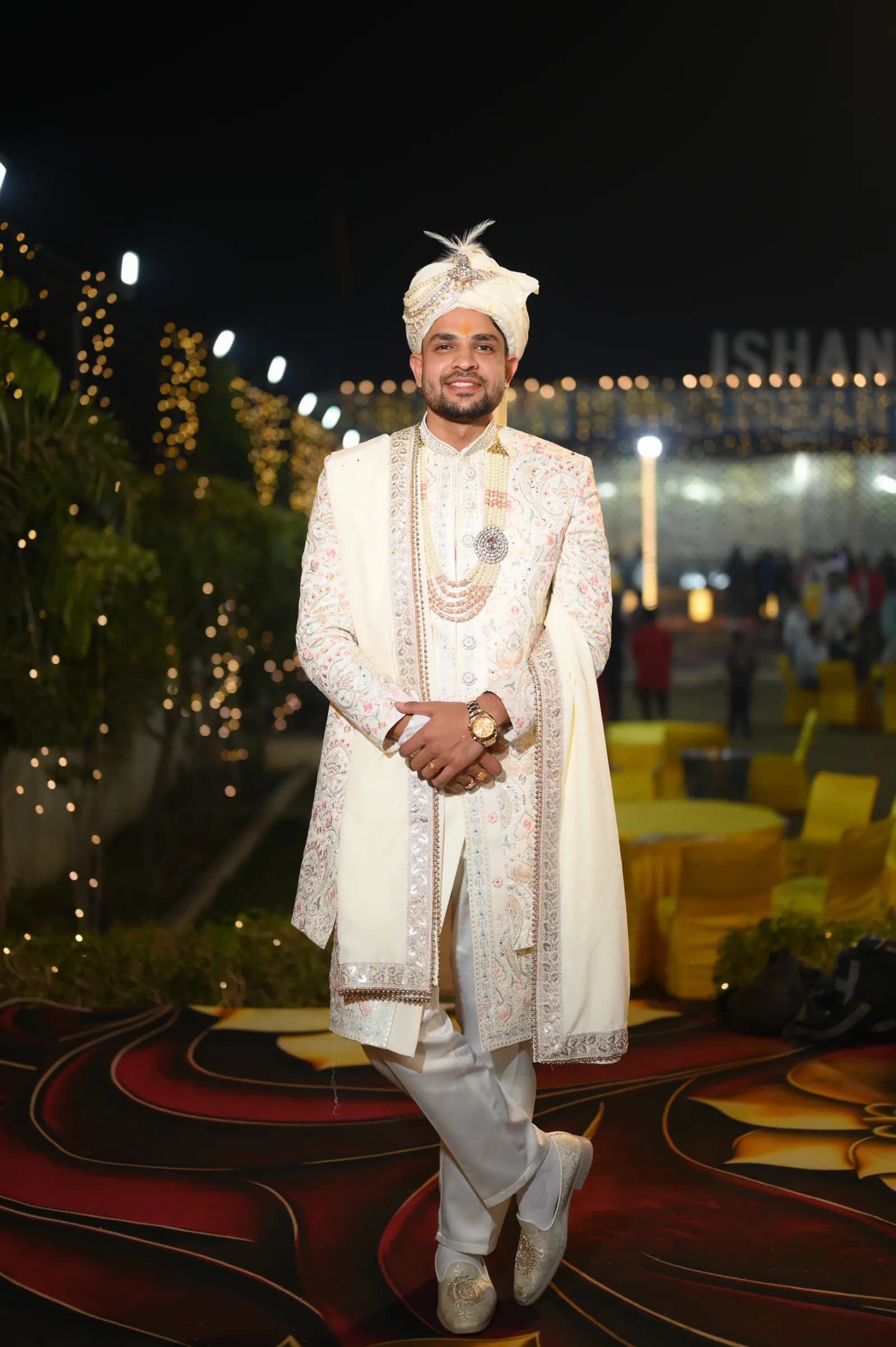 Groom in an ivory sherwani and safa posing at a lit-up night venue