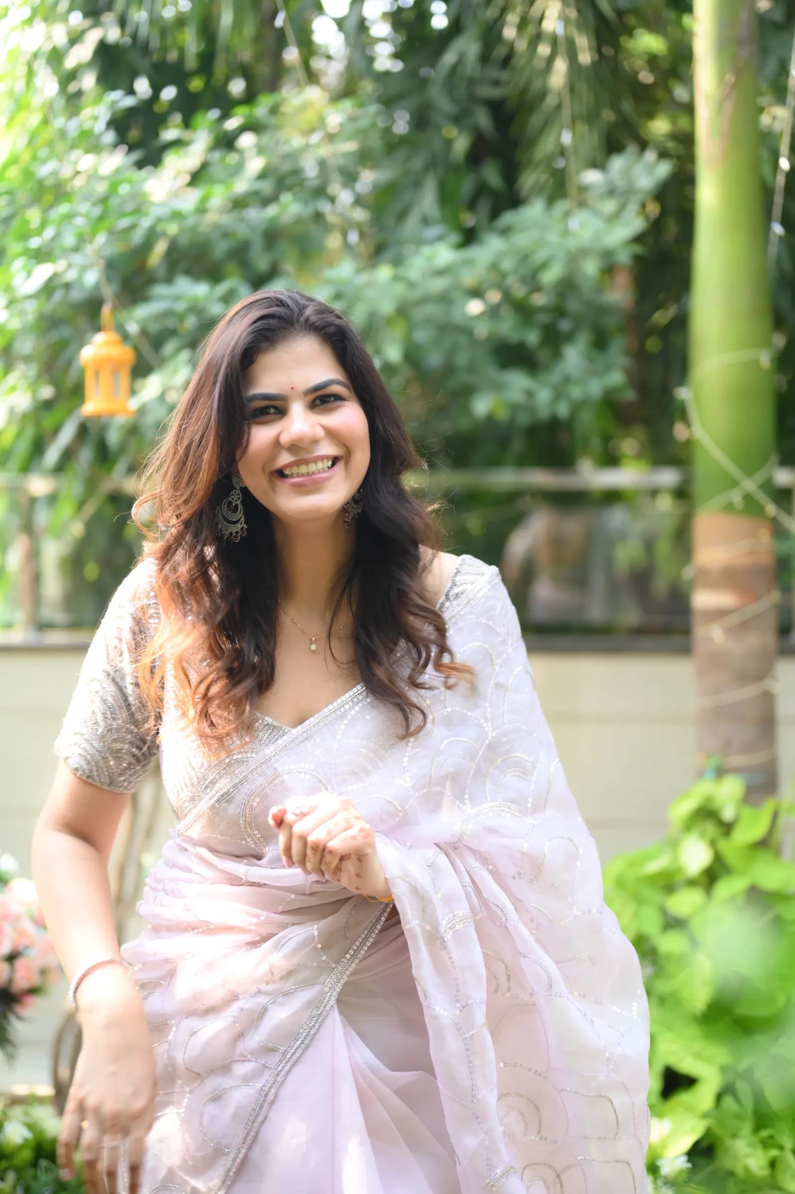 Woman in a white saree laughing in a lush garden