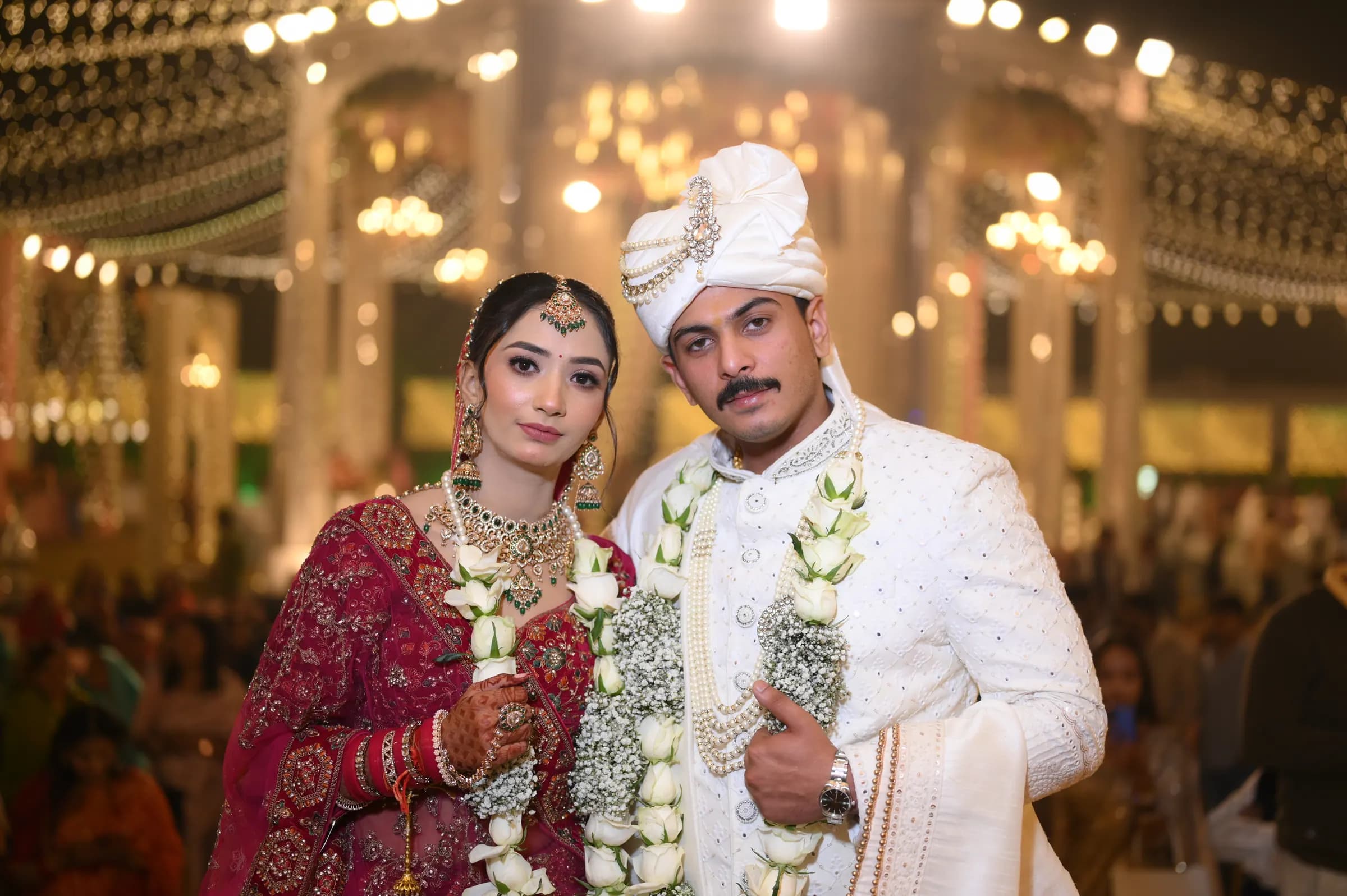 Couple wearing varmala garlands at a lit-up wedding venue at night