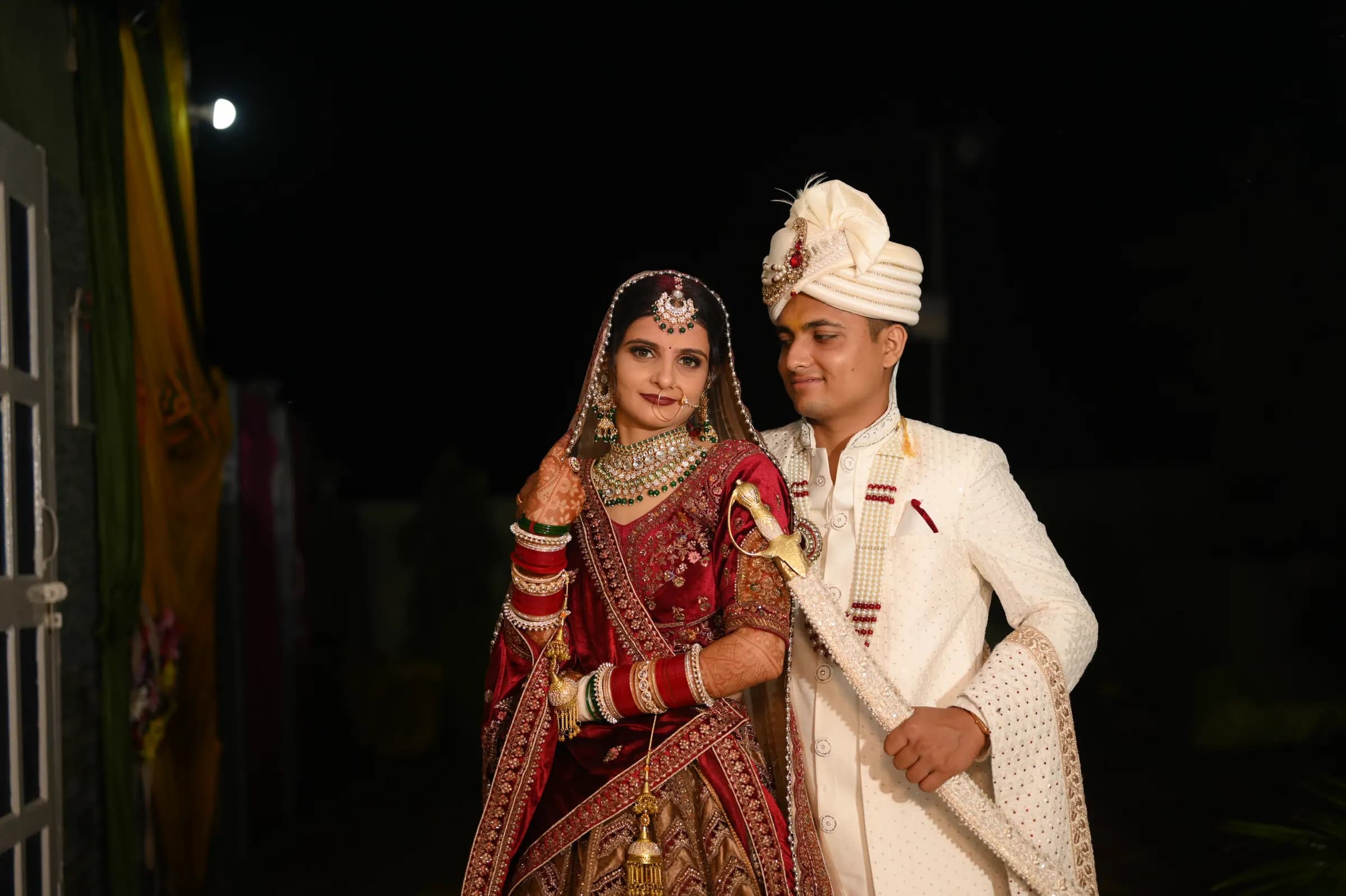 Groom holding a ceremonial sword beside the bride in a night portrait