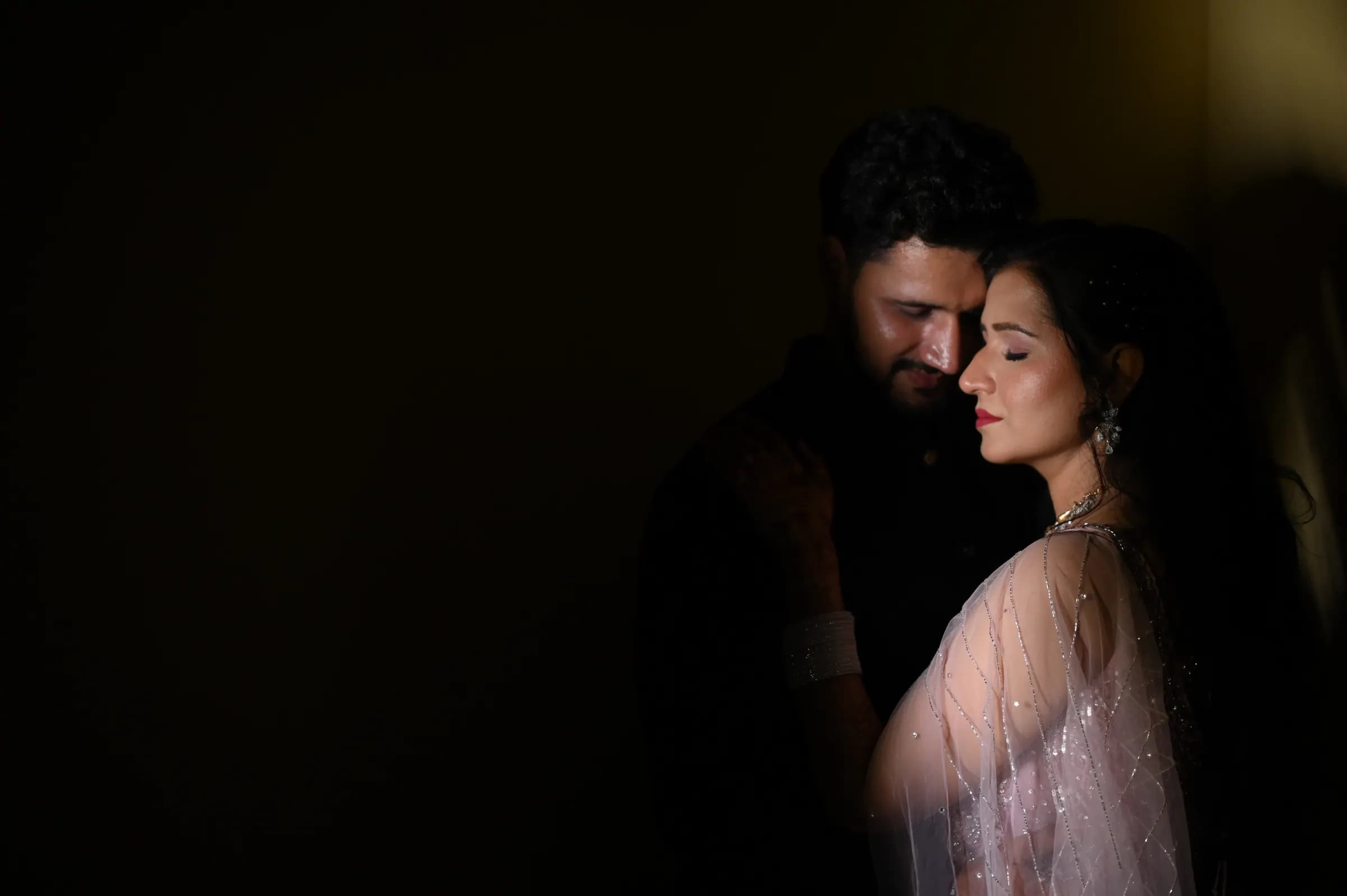 Low-key couple portrait, the bride resting her head close to the groom in soft light